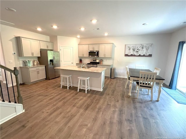 kitchen featuring a breakfast bar area, dark wood-style flooring, appliances with stainless steel finishes, a center island with sink, and recessed lighting