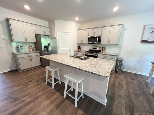 kitchen with a breakfast bar area, an island with sink, dark wood-type flooring, a sink, and appliances with stainless steel finishes