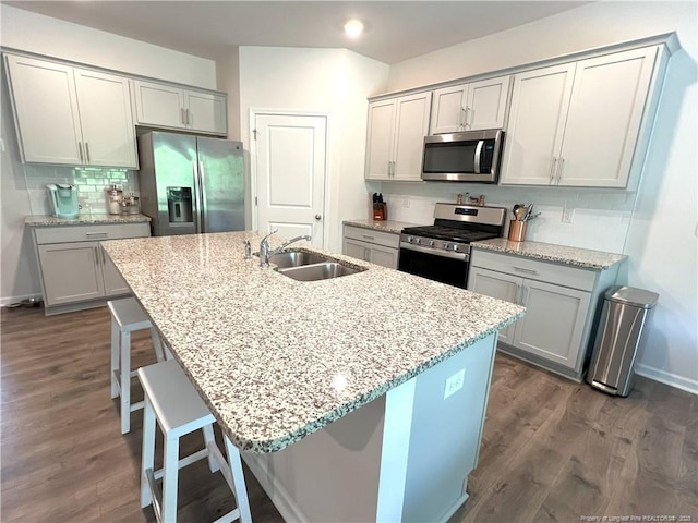 kitchen featuring a sink, appliances with stainless steel finishes, a kitchen breakfast bar, and dark wood-style floors