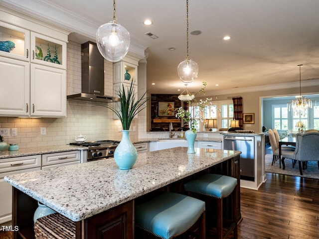 kitchen with wall chimney range hood, a center island, ornamental molding, a peninsula, and a chandelier