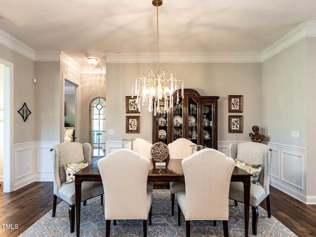 dining room featuring dark wood finished floors, crown molding, a chandelier, a wainscoted wall, and a decorative wall