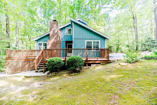 exterior space with board and batten siding, a wooded view, a chimney, and a wooden deck