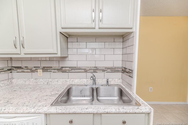 kitchen with decorative backsplash, light tile patterned flooring, baseboards, white cabinets, and a sink