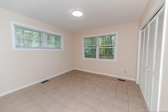 unfurnished bedroom with light tile patterned floors, baseboards, a closet, and visible vents