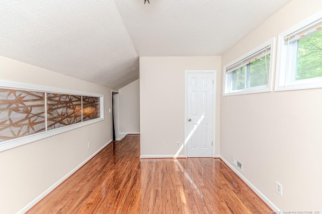 spare room featuring baseboards, a textured ceiling, wood finished floors, and vaulted ceiling
