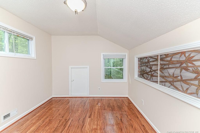 unfurnished room with plenty of natural light, vaulted ceiling, light wood finished floors, and visible vents