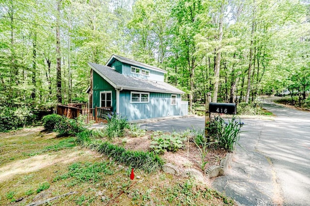 view of property exterior with a wooden deck, a shingled roof, driveway, and a wooded view
