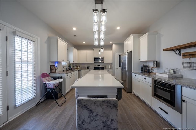 kitchen featuring appliances with stainless steel finishes, hanging light fixtures, a sink, dark wood finished floors, and white cabinetry