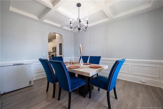 dining room featuring an inviting chandelier, arched walkways, coffered ceiling, and wood finished floors