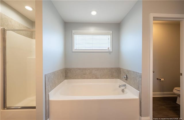 bathroom with a shower stall, toilet, a bath, and wood finished floors