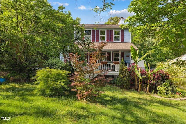 view of front of house featuring covered porch, a chimney, and a front yard