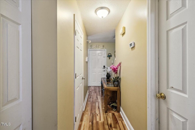 hall with a textured ceiling, baseboards, and light wood-type flooring