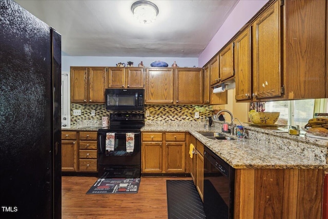 kitchen featuring a sink, brown cabinets, black appliances, and dark wood-style floors