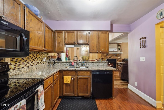 kitchen featuring brown cabinetry, a sink, baseboards, black appliances, and dark wood-style floors