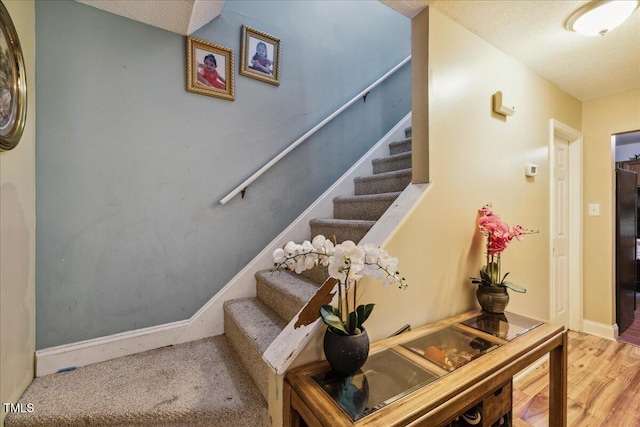 stairway featuring a textured ceiling, baseboards, and wood finished floors