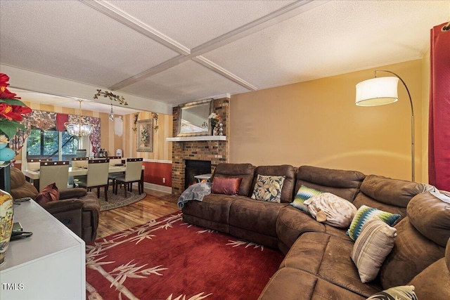 living area with a textured ceiling, a brick fireplace, beam ceiling, wood finished floors, and an inviting chandelier