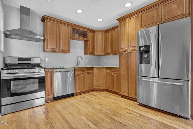 kitchen featuring wall chimney range hood, appliances with stainless steel finishes, brown cabinets, light wood-style floors, and recessed lighting