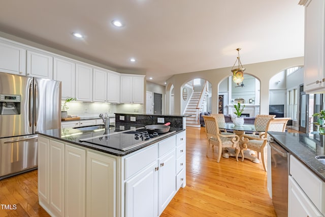 kitchen with white cabinets, a sink, arched walkways, light wood-style flooring, and stainless steel appliances