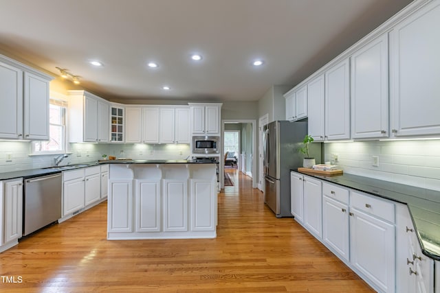 kitchen featuring white cabinets, dark countertops, stainless steel appliances, decorative backsplash, and a kitchen island