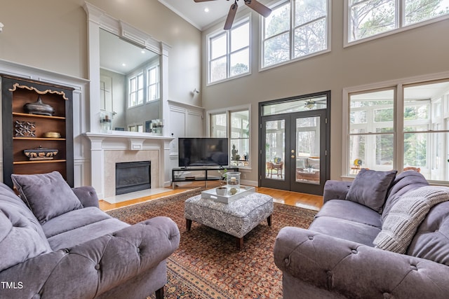 living area featuring crown molding, a towering ceiling, french doors, a ceiling fan, and a high end fireplace