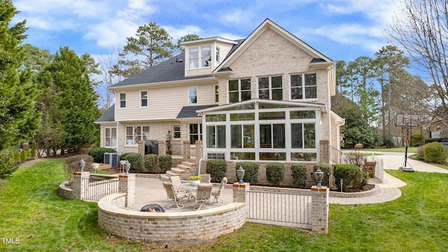 rear view of property with a sunroom, a patio area, a lawn, and brick siding