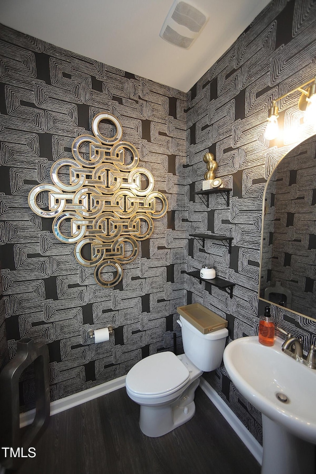 half bathroom featuring toilet, visible vents, a sink, and wood finished floors