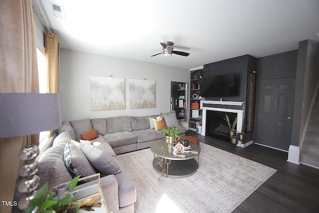 living area featuring dark wood-style flooring, a ceiling fan, a fireplace with flush hearth, and visible vents