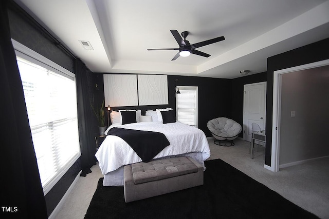 bedroom featuring a ceiling fan, visible vents, a raised ceiling, baseboards, and carpet