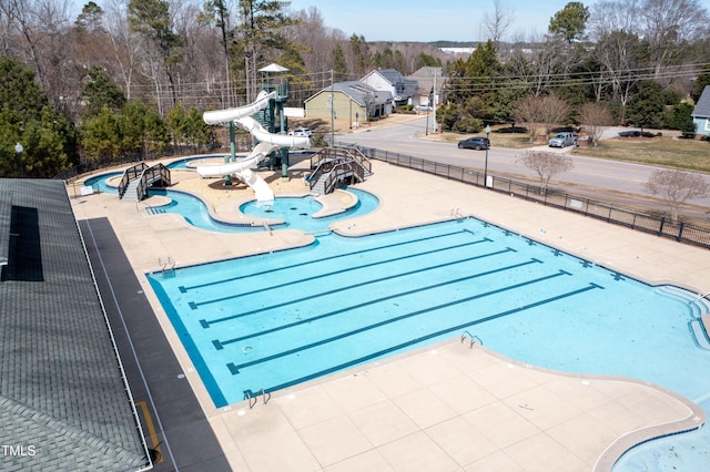 community pool with fence, a water slide, and a patio area
