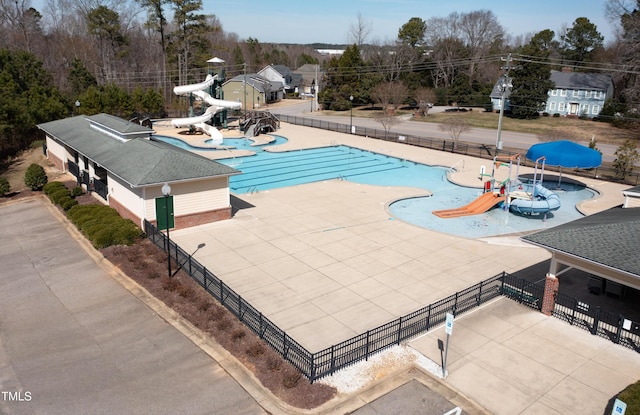 community pool with fence, a water slide, a patio area, and a water play area