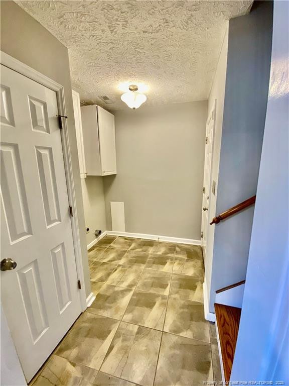 laundry area with baseboards, a textured ceiling, and cabinet space