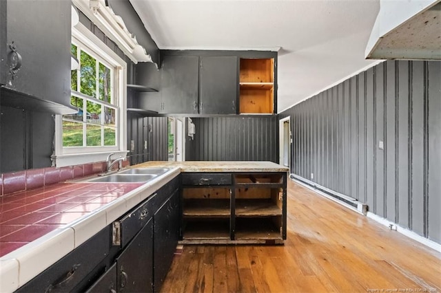 kitchen featuring a sink, light wood-style floors, open shelves, and tile countertops