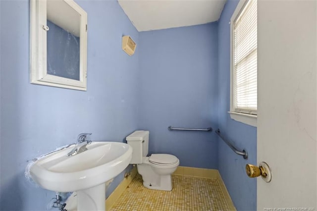 half bath with a sink, tile patterned floors, baseboards, and toilet