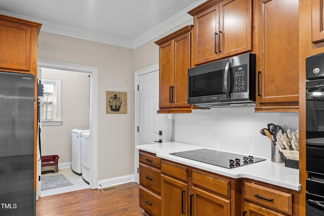 200 Heather Brook Cir, Spring Lake, NC 28390 - kitchen featuring independent washer and dryer, black electric cooktop, freestanding refrigerator, tasteful backsplash, and ornamental molding
