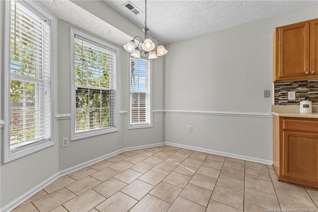 unfurnished dining area with a textured ceiling, a chandelier, baseboards, light tile patterned floors, and visible vents