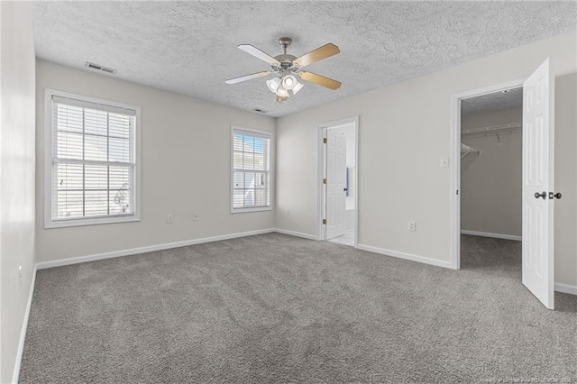 unfurnished bedroom with a walk in closet, baseboards, a textured ceiling, and visible vents