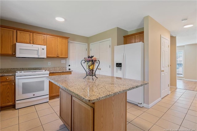 kitchen featuring light tile patterned floors, light stone countertops, a kitchen island, and white appliances
