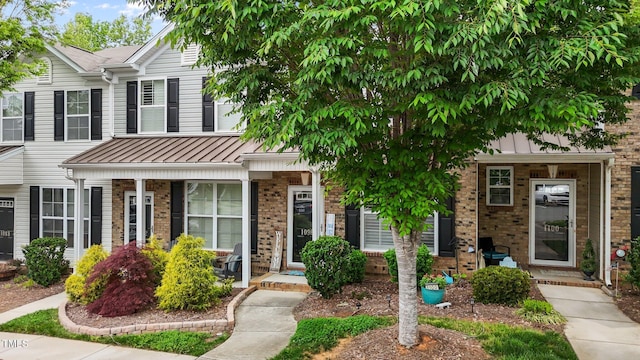 townhome / multi-family property with covered porch, brick siding, a standing seam roof, and metal roof