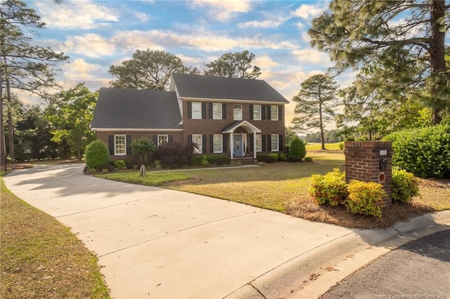 colonial house featuring brick siding, driveway, and a front lawn