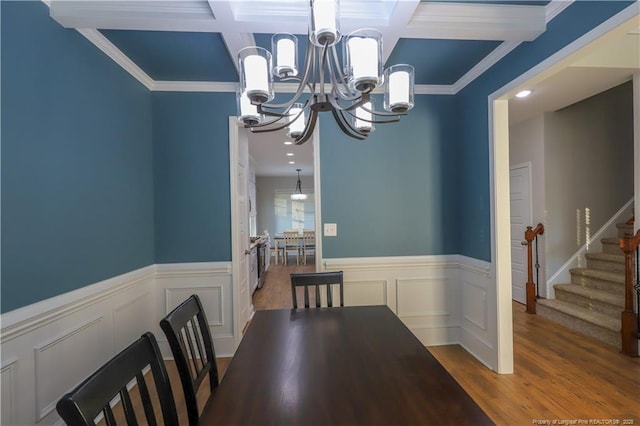 dining room with a decorative wall, a chandelier, a wainscoted wall, stairs, and coffered ceiling
