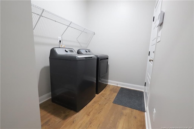 washroom with laundry area, washing machine and dryer, baseboards, and light wood finished floors