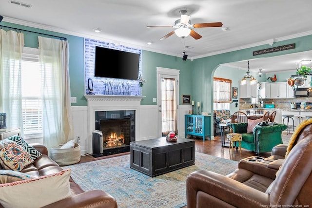 6628 Carriage Crossing Rd, Hope Mills, NC 28348 - living area featuring a lit fireplace, a ceiling fan, arched walkways, light wood-style floors, and ornamental molding