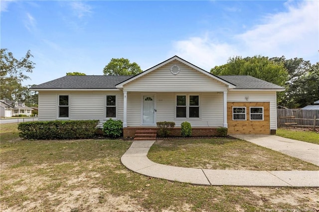 view of front of property with covered porch, fence, a shingled roof, and a front yard
