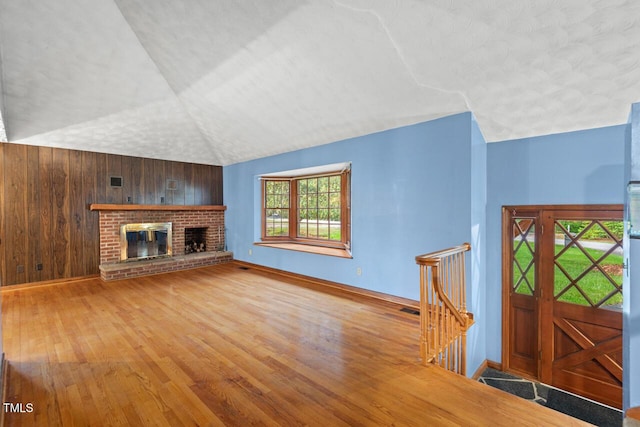 unfurnished living room featuring a fireplace, vaulted ceiling, wood walls, baseboards, and wood-type flooring