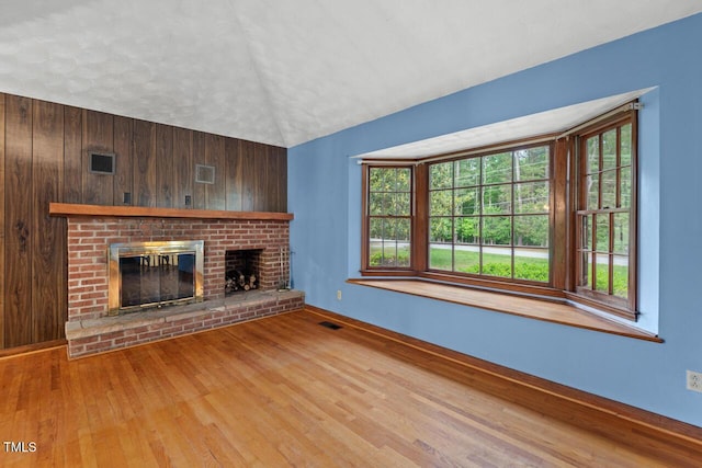 unfurnished living room featuring visible vents, a brick fireplace, hardwood / wood-style floors, baseboards, and vaulted ceiling