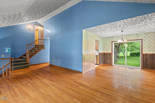 unfurnished living room featuring wallpapered walls, a chandelier, wood finished floors, and a wainscoted wall