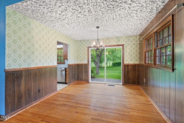 unfurnished dining area featuring a wainscoted wall, wallpapered walls, hardwood / wood-style flooring, and a notable chandelier