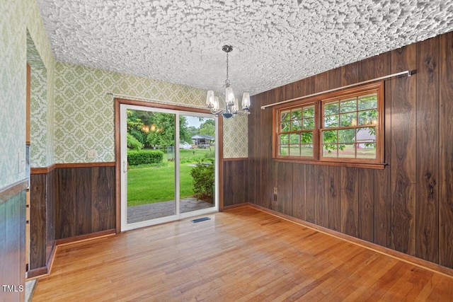unfurnished dining area with visible vents, wood-type flooring, wood walls, and a chandelier