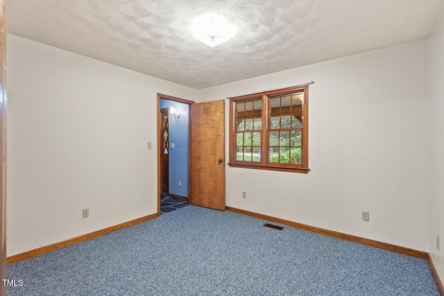 empty room with carpet floors, a textured ceiling, baseboards, and visible vents
