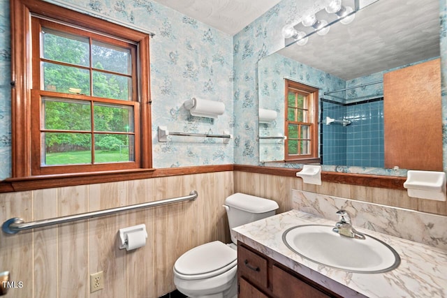 bathroom featuring vanity, wainscoting, a shower, toilet, and wallpapered walls